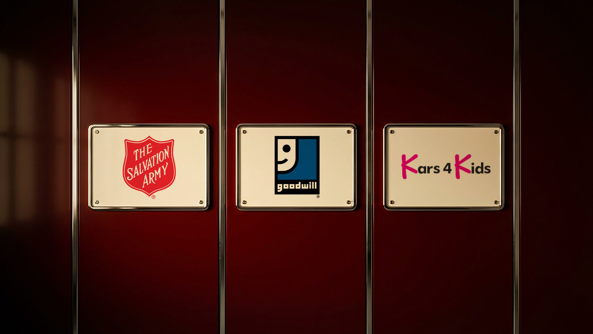 Plaques on a deep red garage wall showing the logos of The Salvation Army, Goodwill and Kars4Kids
