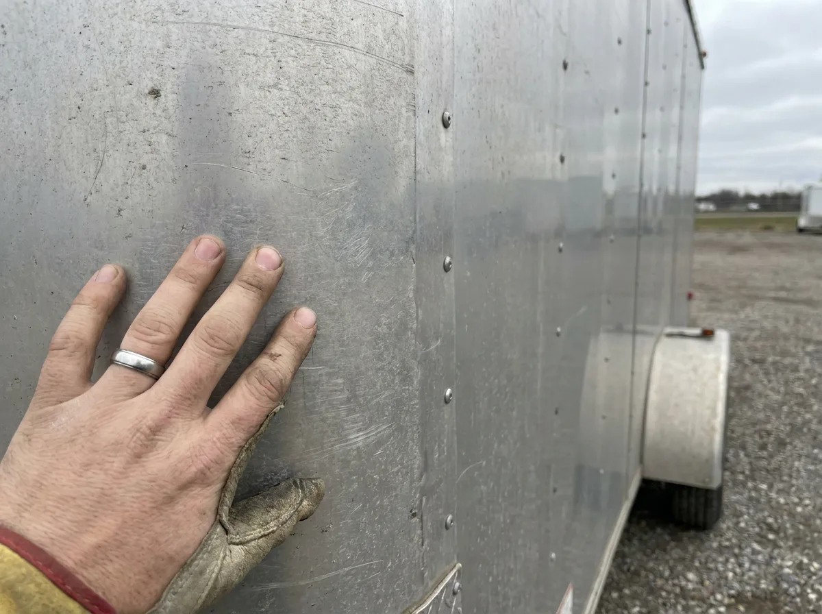 Hand touching ribbed aluminum side panel of cargo trailer in daylight