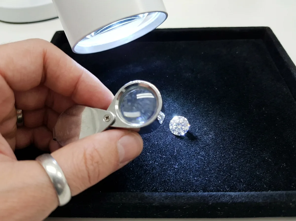 Jeweler's loupe examining loose diamond on black velvet tray under bright light