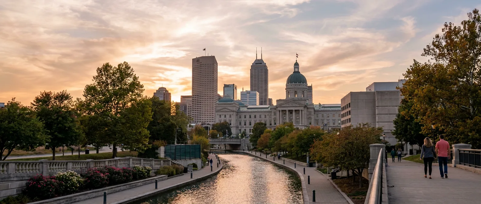 Indianapolis skyline at dusk with warm sunlight reflecting over a canal bordered by trees